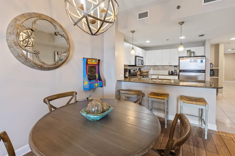 Your open-concept space blends dining and kitchen seamlessly, with modern appliances and charming details like the vintage arcade game for entertainment.