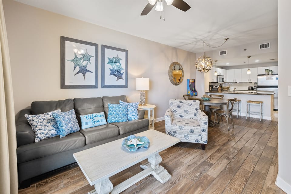 Relax in your coastal-themed living space with ocean artwork and comfortable seating flowing into a fully equipped kitchen.