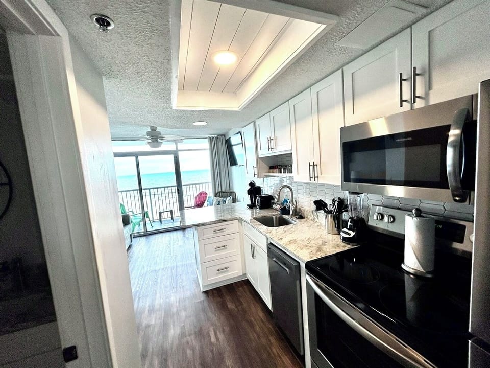 Bright kitchen w/ stainless steel appliances, granite counters & balcony views just beyond.
