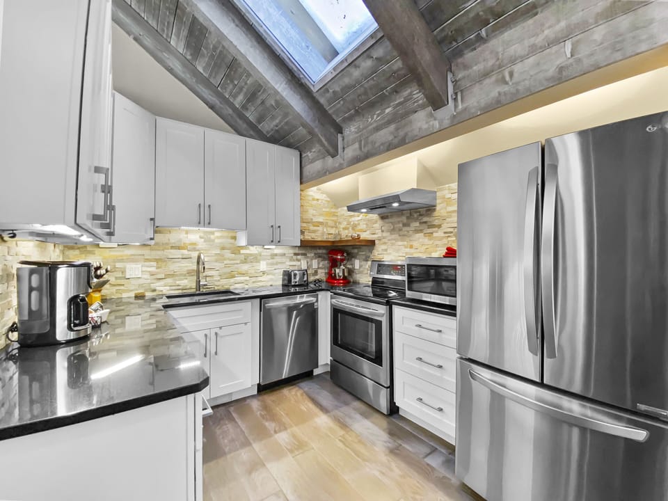 A modern kitchen with stainless steel appliances, white cabinetry, stone backsplash, and a skylight.
