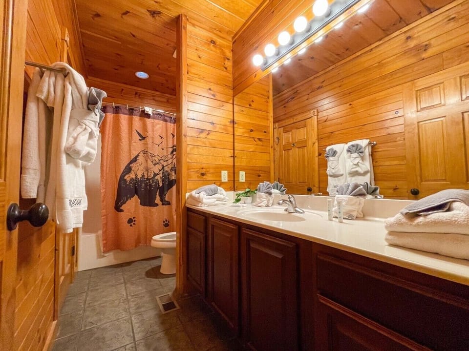 Full bathroom with double vanity, bear shower curtain, and robes — one per level