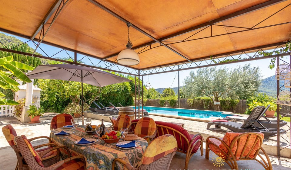 Covered outdoor dining area with table for several guests, located next to the private swimming pool and surrounded by Mediterranean garden.