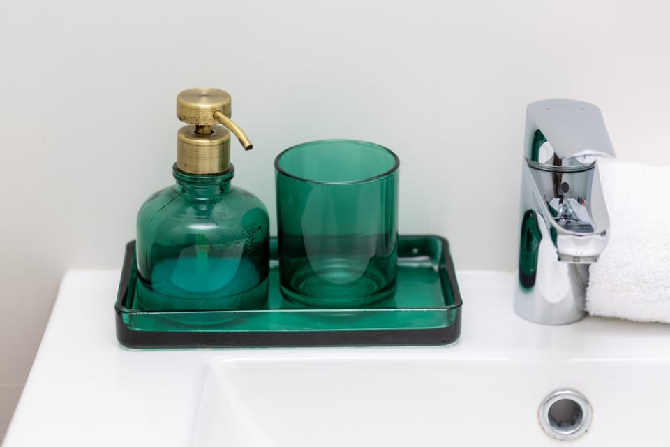 A stylish bathroom counter with green glass containers and a luxurious feel.

