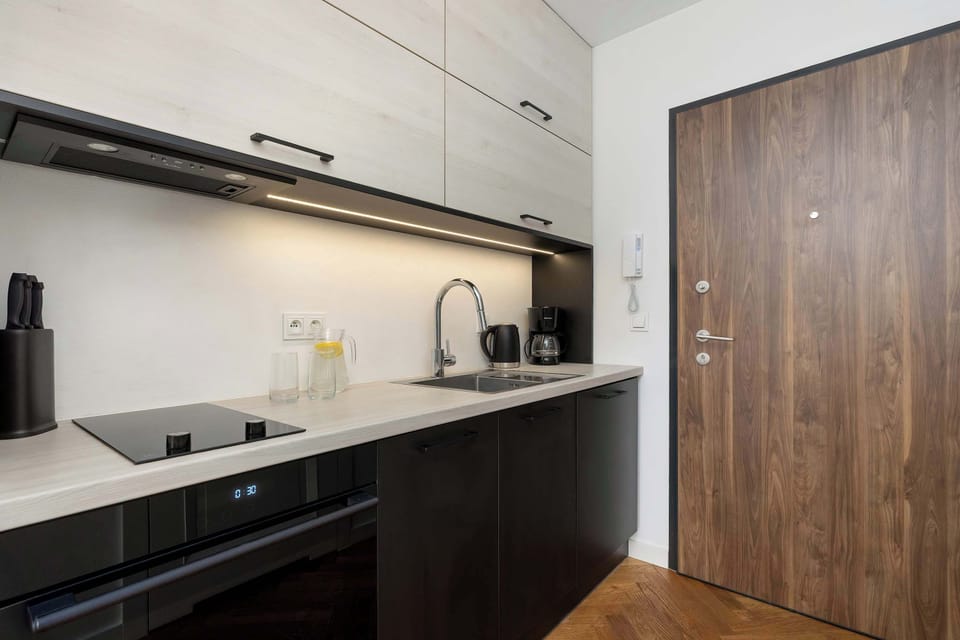 A contemporary kitchenette with subtle under-cabinet lighting. A wooden door leads into the adjacent room.