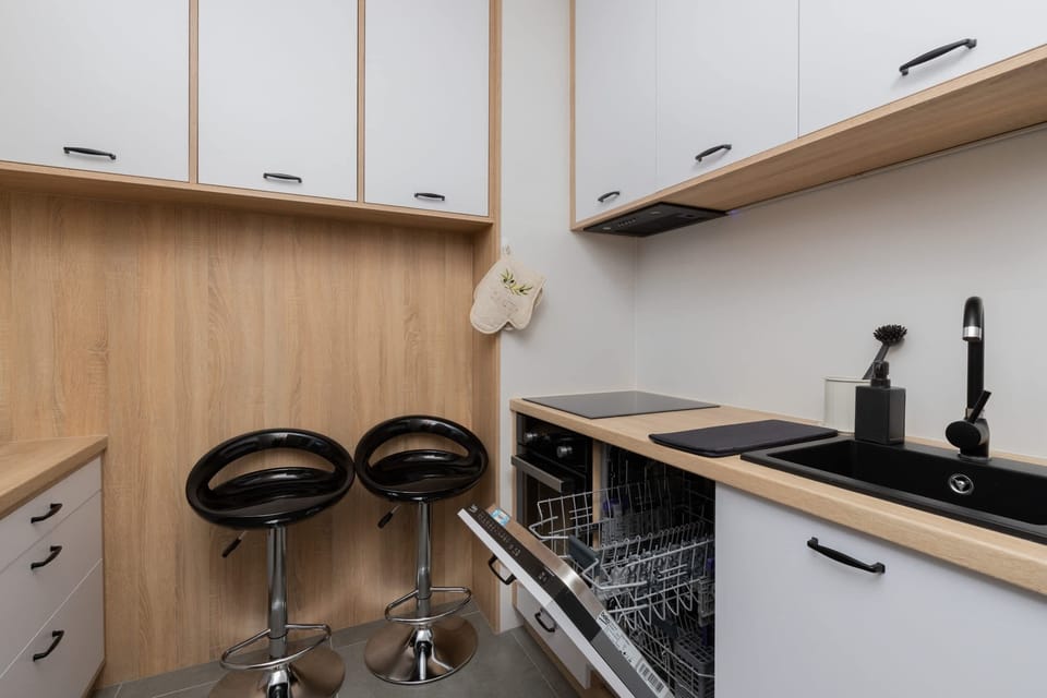 A compact kitchen featuring modern appliances, white cabinets, and a neutral wooden countertop.
