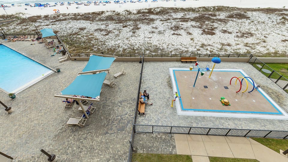 Colorful water sprayers splash as kids play beside the pool while you watch from shaded seating nearby