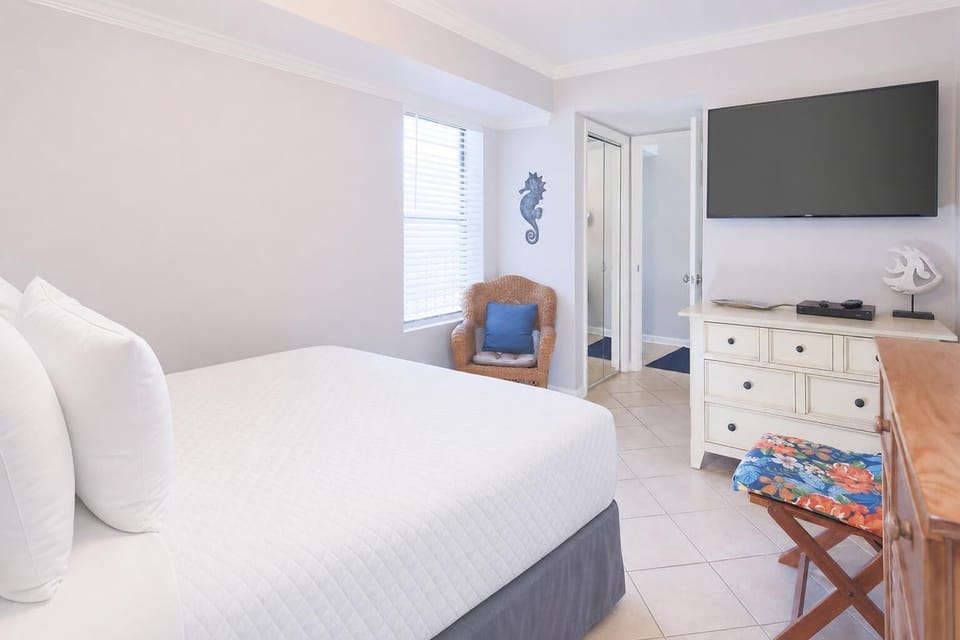 The guest bedroom features a cozy chair by the window, a large TV, and a stylish dresser, perfect for relaxation