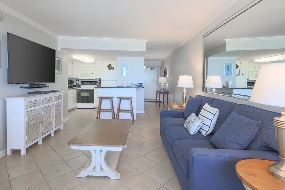 The living area features a comfortable sofa, a large TV, and a view into the well-equipped kitchen, perfect for relaxation