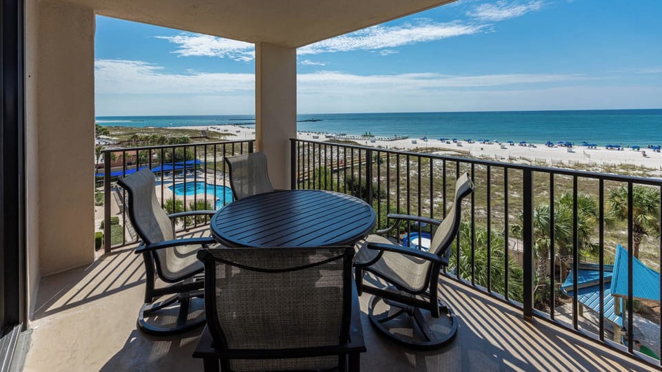 Relax on the balcony enjoying views of the beach and pool area under the bright blue sky