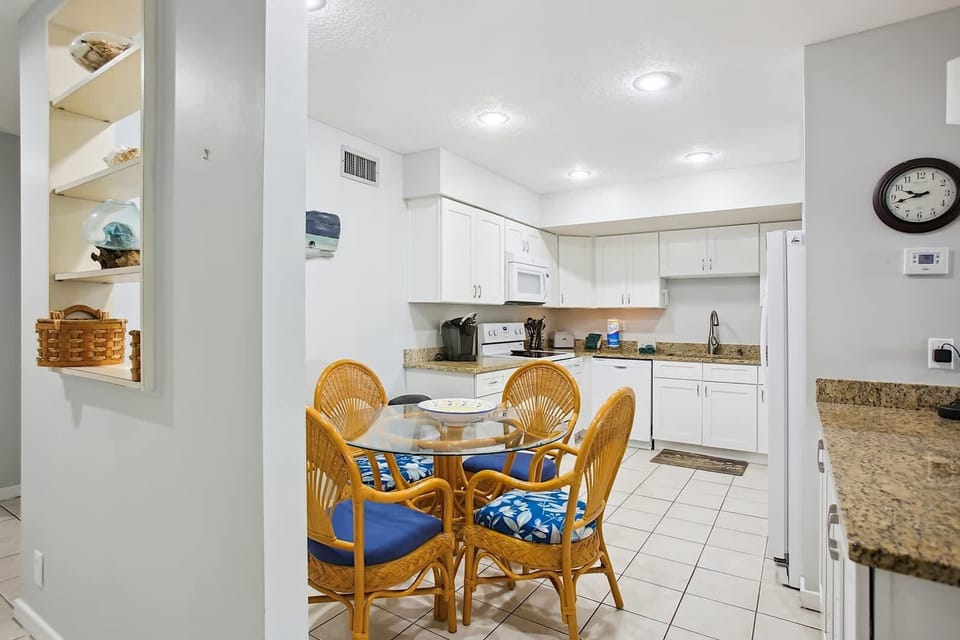 - Bright white kitchen with granite counters and a round glass table for casual meals
- Rattan chairs with blue cushions tie in the coastal theme beautifully
- Fully equipped for cooking with all essentials for longer stays