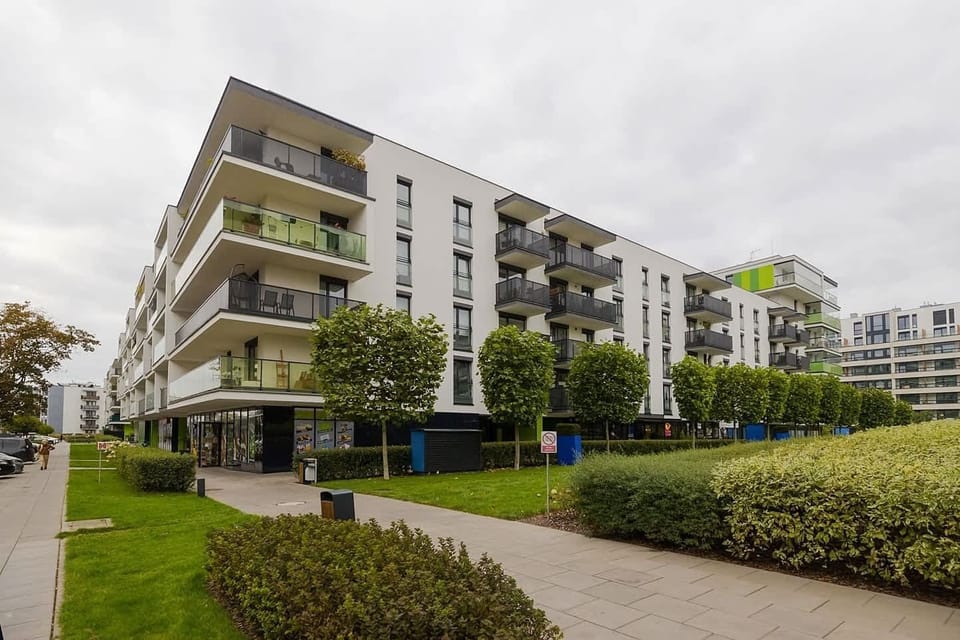 A modern apartment building with vibrant green accents, surrounded by well-kept gardens and pathways.
