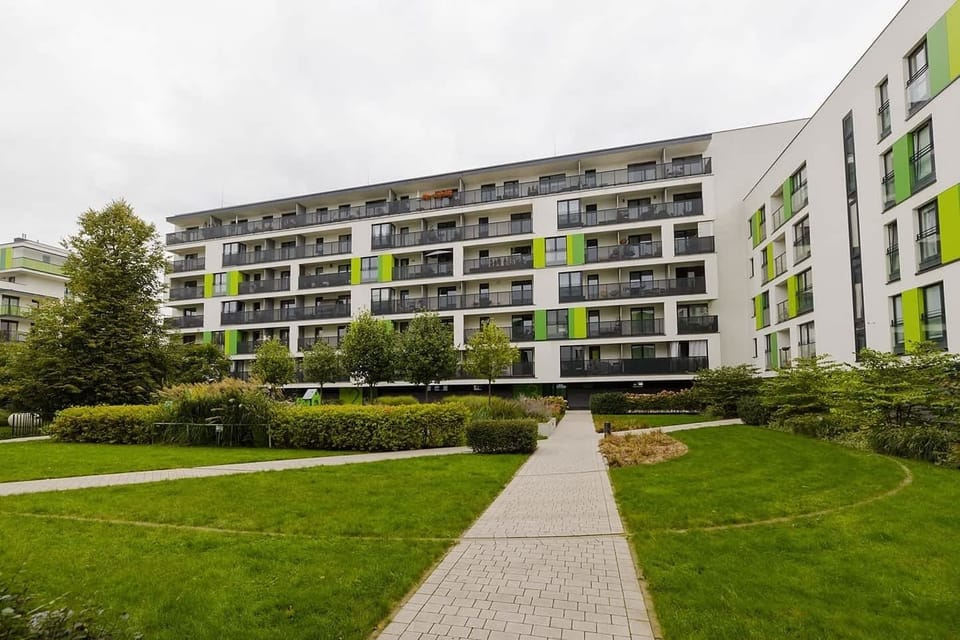A modern apartment building with vibrant green accents, surrounded by well-kept gardens and pathways.