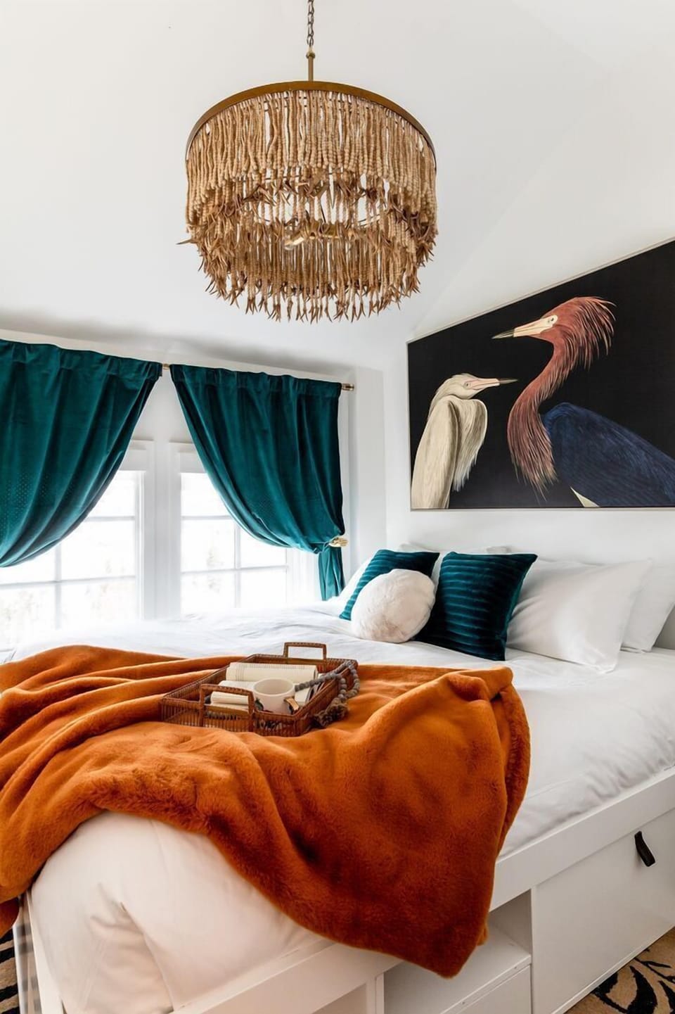 This bedroom has a king bed with red-colored throw, decorative pillows, and framed artwork.