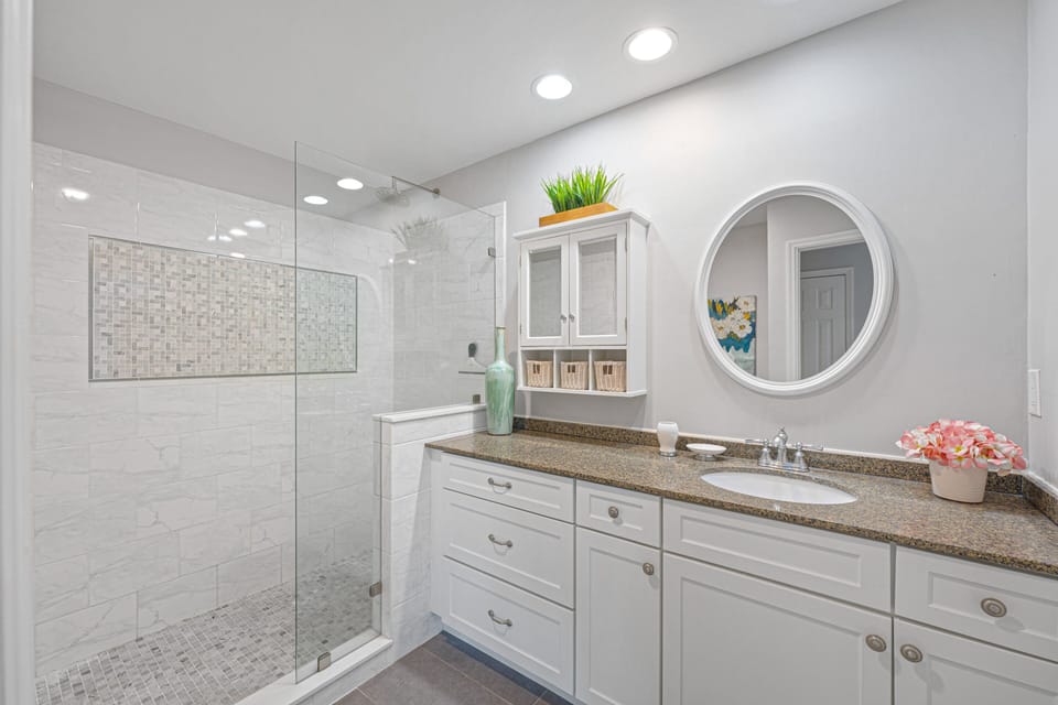 The walk-in glass shower showcases elegant tilework with a decorative inset and built-in bench, paired with modern fixtures and ample storage.