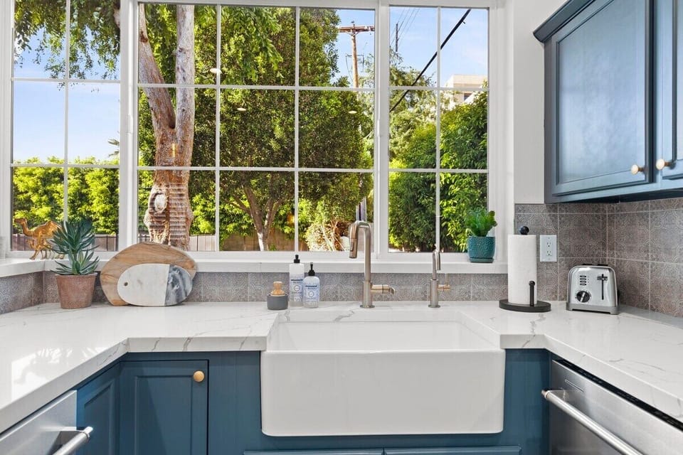 Farmhouse kitchen sink with quartz countertops with large picture window into the backyard with mature trees and pool