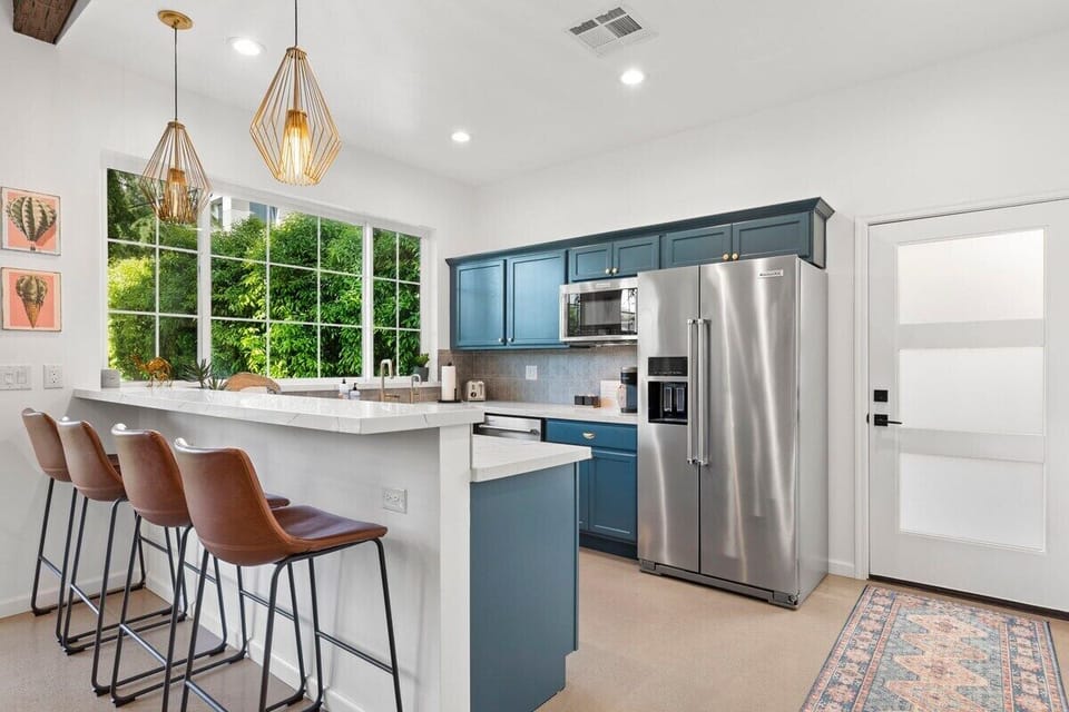 Modern kitchen with stainless steel appliances, quartz countertops, high top seating, pendant lights and backyard view