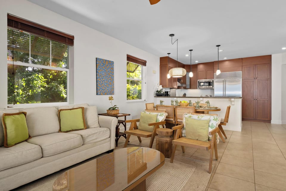 Your bright, open living space flows seamlessly from cozy seating to modern kitchen, with tropical garden views framing every moment.