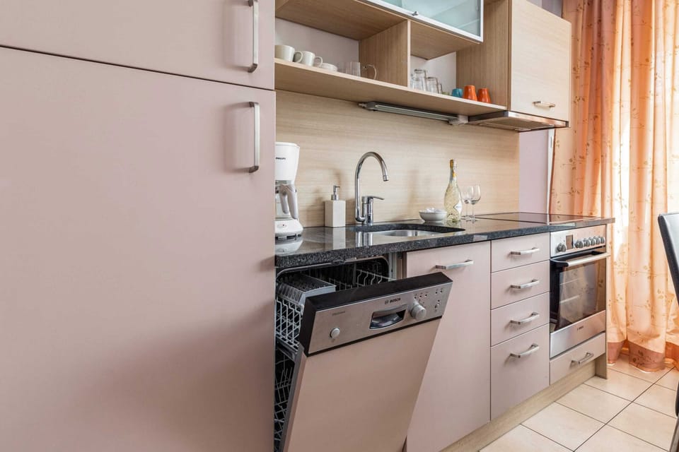 A kitchen area with a sink, stove, oven, and cabinets in a light brown color.