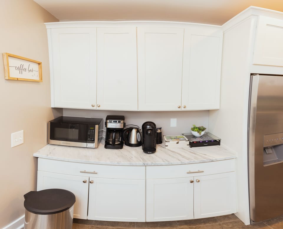Coffee bar stocked with a drip coffee machine, kettle, Nespresso frother & pods.