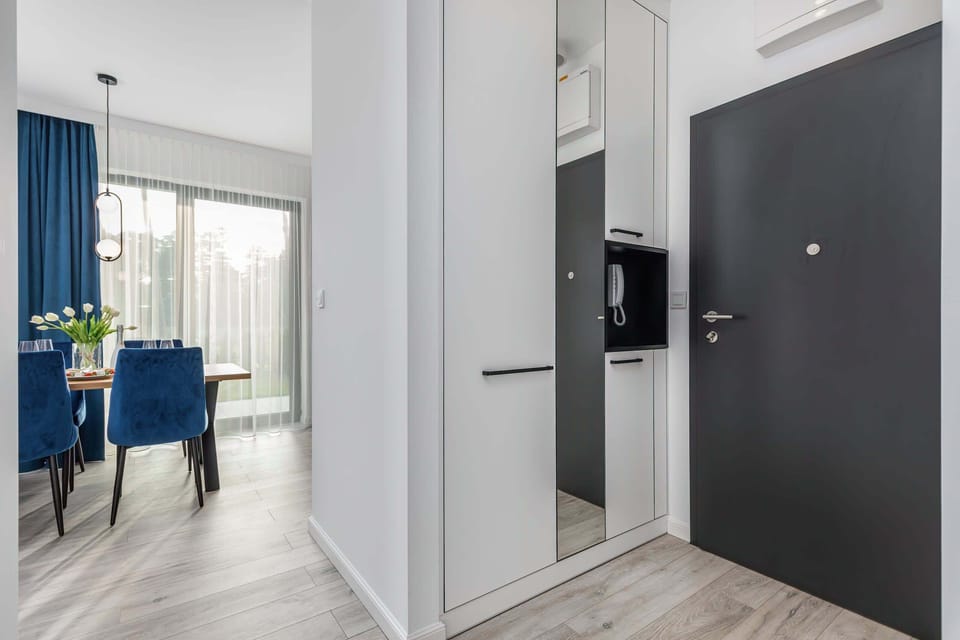 Hallway leading to a living area, with blue curtains visible in the background and sleek white walls.