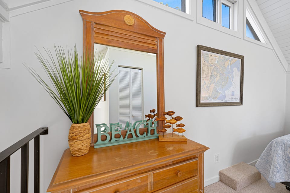 This inviting corner adds a warm, beach-inspired touch with a classic wood dresser, framed mirror, and tasteful coastal accents.