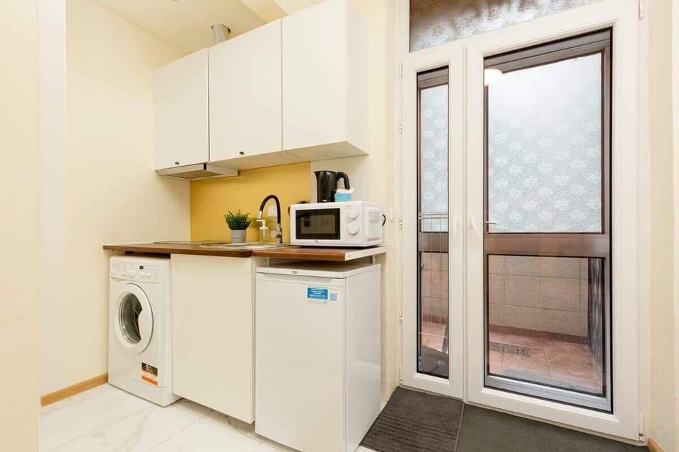 A compact kitchen with white cabinets and essential appliances, including a microwave and kettle.
