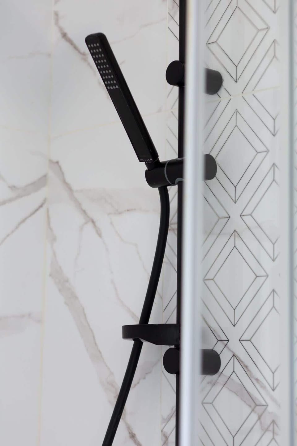 A close-up of the shower, showcasing a sleek black rain showerhead and glass doors.
