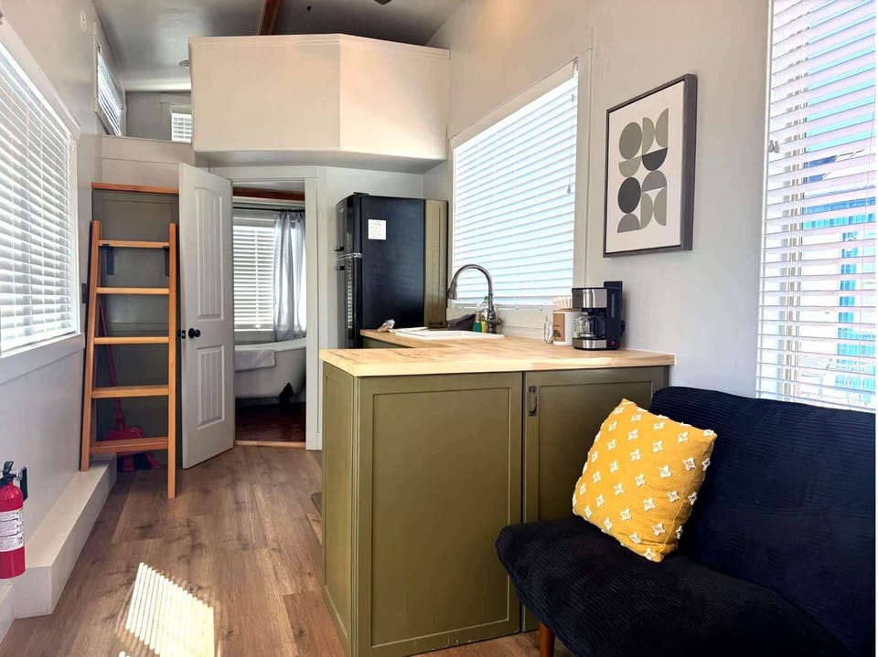 Cozy kitchen and lounge area with retro-style fridge, dining nook, loft ladder access, and comfortable seating in this modern tiny home retreat.