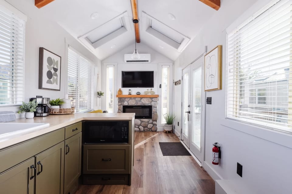 Spacious open-concept tiny home interior featuring vaulted ceilings, skylights, modern kitchen, fireplace, Smart TV, and cozy living space.