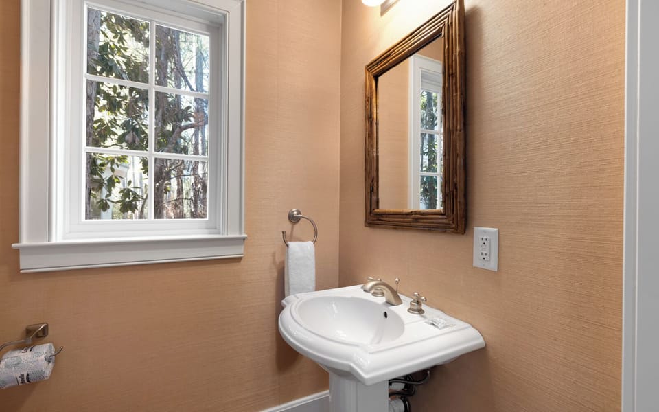 Freshen up in your elegant powder room featuring a classic pedestal sink, warm natural lighting, and charming garden views.