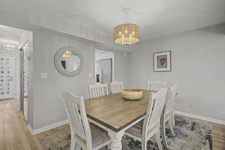 Gather around your elegant dining table where warm conversations flow under coastal-inspired chandelier light and soft natural tones create perfect dinner memories.