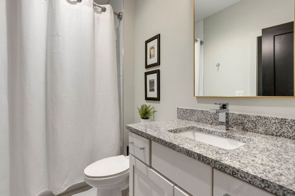 A clean modern bathroom with dark tile accents, granite vanity, and excellent lighting.