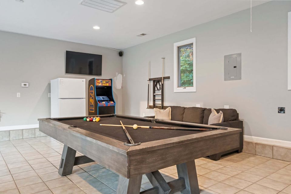 Lower Level game room with pool table, arcade game, couch & TV.
