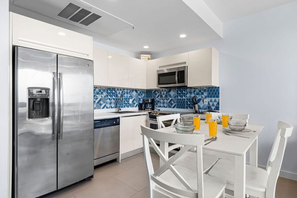 Your modern kitchen awaits with stainless steel appliances, stylish blue geometric backsplash, and a bright dining nook—perfect for preparing meals and enjoying morning coffee together.