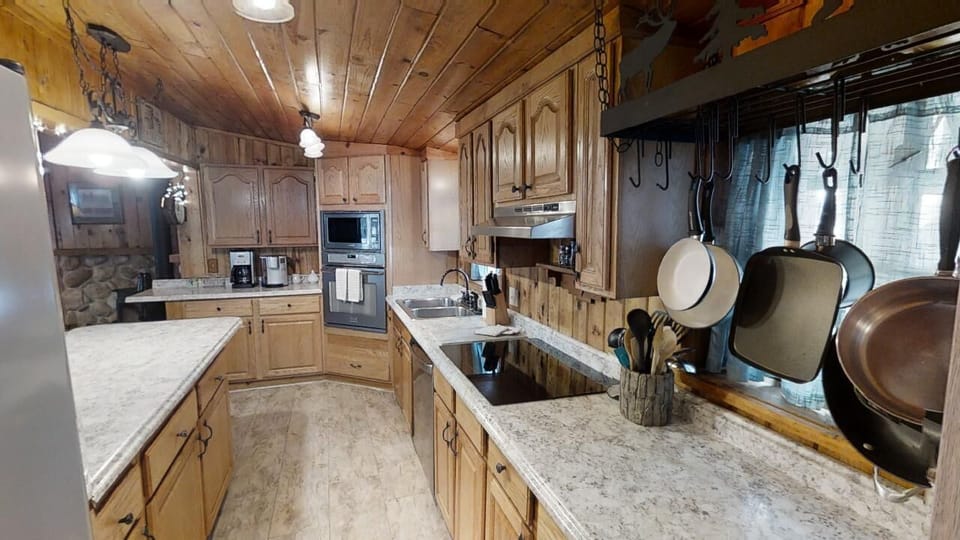 Step into your fully equipped kitchen with rustic charm, featuring granite countertops, modern appliances, and hanging cookware ready for your mountain retreat meals.
