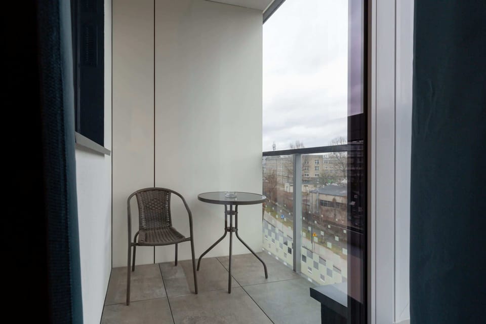 An inviting outdoor balcony equipped with comfortable chairs and a table, providing a perfect spot for enjoying morning coffee or evening drinks while taking in panoramic city views.

