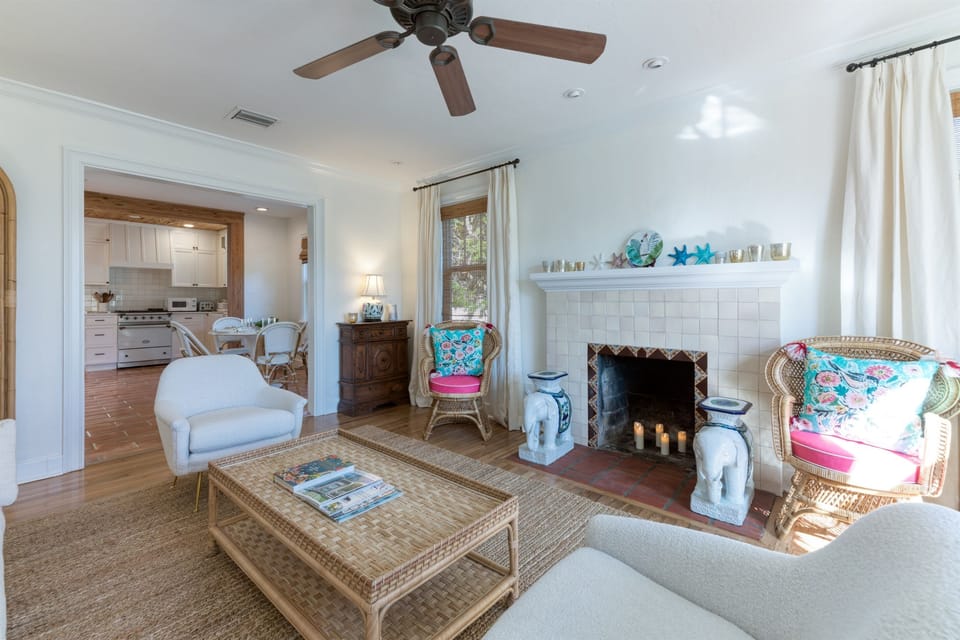The charming house features a comfortable living room area with an off-white sofa, two rattan arm chairs alongside the original decorative (non-working) fireplace and two white armchairs that sit on a hand woven farmhouse rug.
