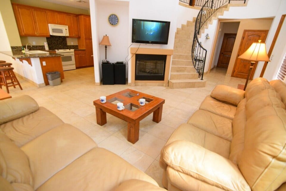 The living room features a flat‑screen TV, high ceilings, and a tile fireplace — steps from the community pool and jacuzzi .