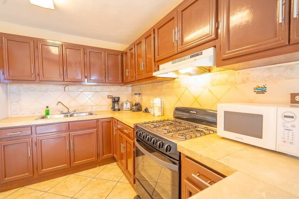 The well-equipped kitchen includes a microwave, full-sized refrigerator, 4-burner stove, oven, and coffee maker — just steps from the beach and a short walk to the Malecon.