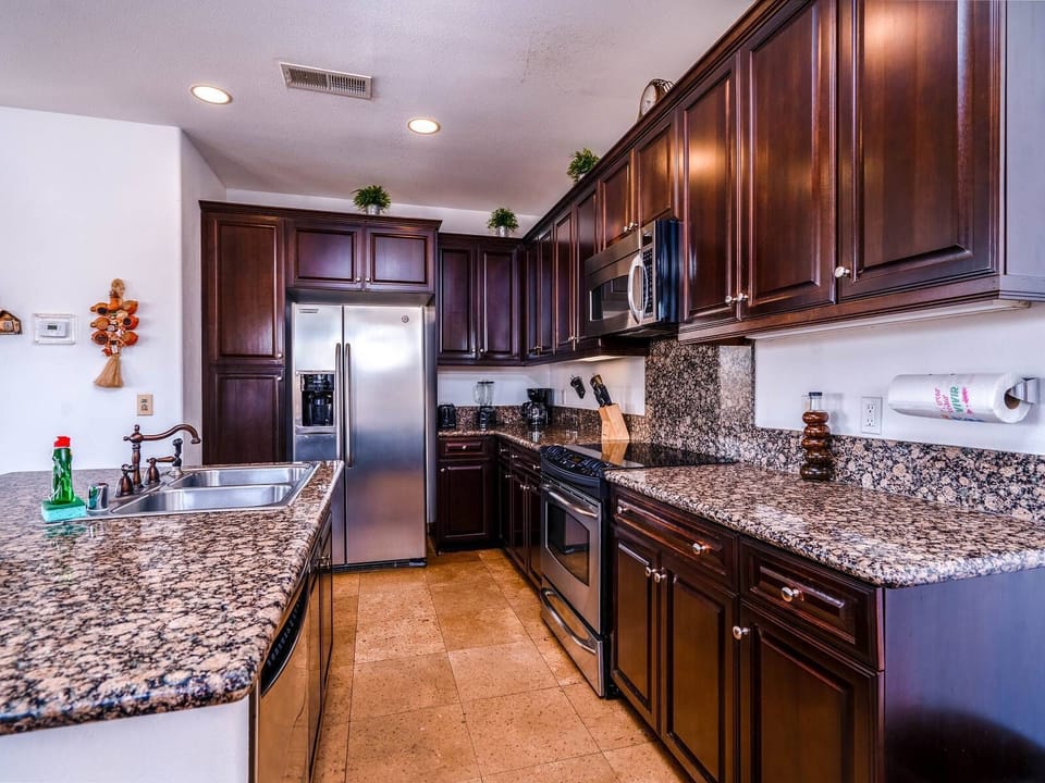 The side view shows the breakfast bar, gas stove, double sinks, and ample counter space — flowing into the living and dining areas.