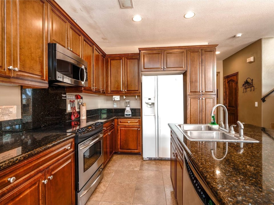 The well-appointed L-shaped kitchen features a double oven, granite island with bar stool seating, and stunning golf course views — as seen in this El Dorado Ranch vacation rental.