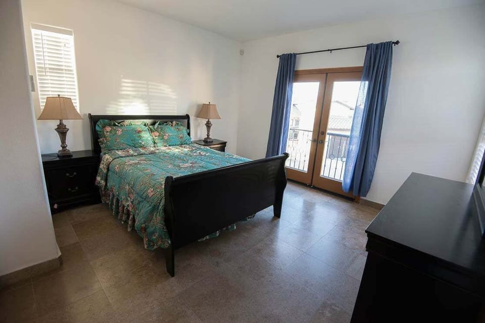 The upstairs master suite features a king bed, private balcony, and an en-suite bathroom with dual sinks and a walk-in shower — overlooking the community pool.