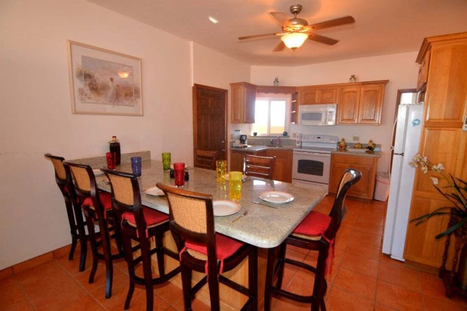 The upstairs kitchen in Condo B features modern appliances, a snack bar with nine bar stools, and flows into the dining and living areas — part of this 4‑bedroom, 4‑bath beach‑side villa .