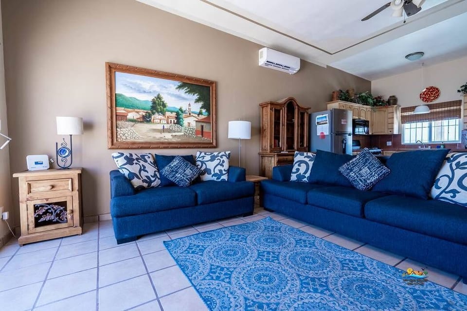 Relax in the sun-filled living room featuring high-end sofas, oversized armchairs, a 42-inch flat-screen TV, and sliding glass doors that open to the ocean-view balcony for fresh sea air