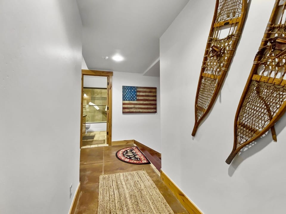 A hallway with a rug on the wooden floor, two snowshoes mounted on the right wall, and an American flag hung at the far end near the entrance to a bathroom. Unit B