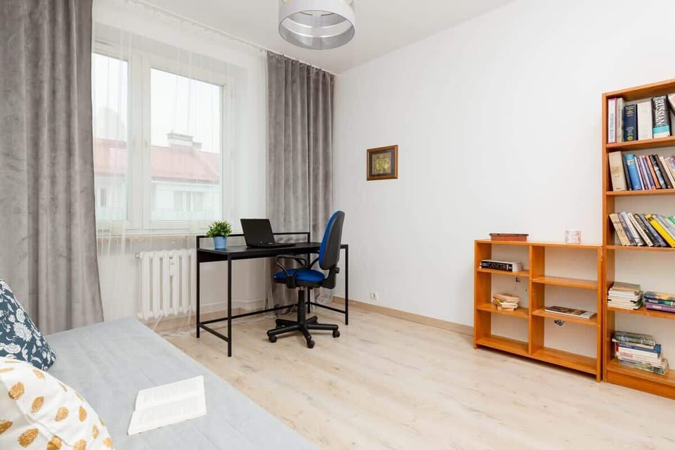 A comfortable bedroom featuring a sofa, a large bookcase, and plenty of natural light for a homely atmosphere.