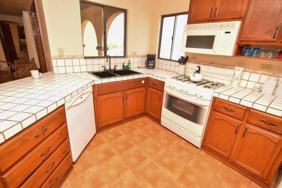 The U-shaped kitchen features extensive granite counter space, double sinks, full-size refrigerator, gas stove, microwave, and dishwasher. Large windows above the sink overlook the private pool area.