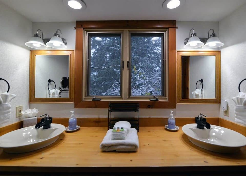 Your spacious dual-vanity bathroom offers perfect morning prep space with warm wood accents and natural forest views.