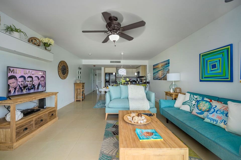 The living room has a TV, a soft and comfortable sofa set, a ceiling fan, and a large sliding door that leads to the balcony.