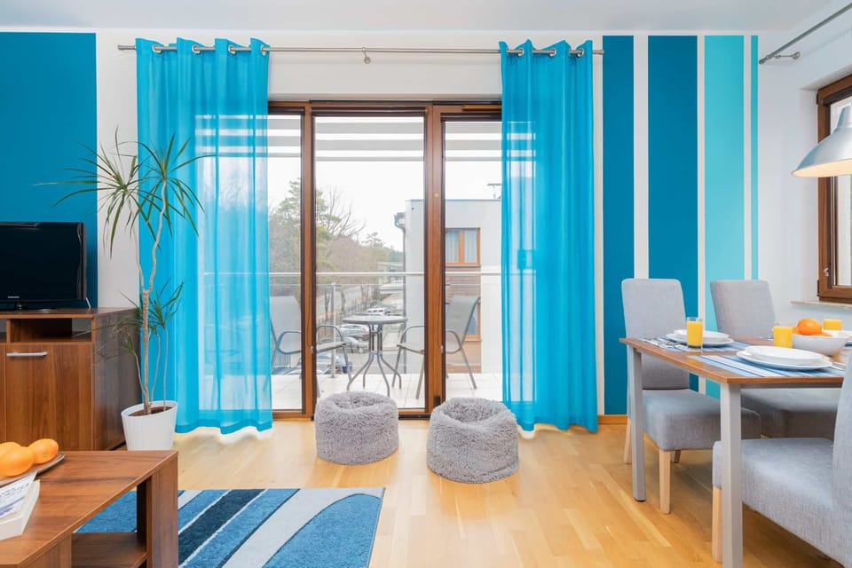 Another angle of the living room showcasing the gray sofa, wooden coffee table, and bright blue walls. The decor includes vibrant accents like green plants.